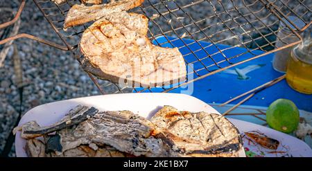 Fette di pesce spada su un piatto bianco e su una griglia barbecue. Messa a fuoco selettiva in primo piano e sfondo sfocato con un frutto di limone e una testa di gamberetti Foto Stock