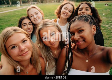 Ragazza adolescente multirazziale sorridente che prende selfie al parco Foto Stock