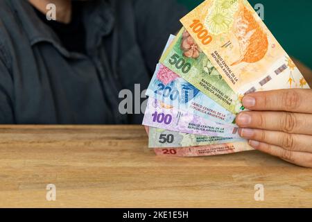 L'uomo dietro la scrivania sta tenendo un pacco di pesos argentini, banconote varie Foto Stock