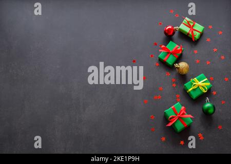 Regali in carta verde con nastri rossi e gialli e palle di natale verdi, dorate e rosse sono sulla destra. Sfondo nero, spazio di copia. Grande vendita conc Foto Stock