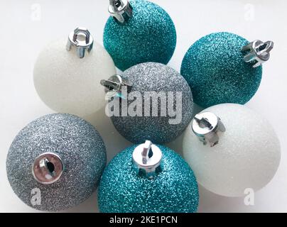 Primo piano di palline di Natale lucenti blu turchese, bianco, argento su sfondo bianco. Il concetto di Natale e Capodanno. Foto Stock