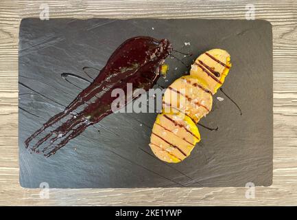 vista dall'alto di un piatto di foie gras fresco su una pietra ardesia, con una marmellata di frutta rossa sul lato e sale grosso, su un tavolo di legno Foto Stock