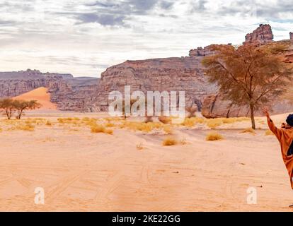 Tadrart Rouge mezzo braccio di sollevamento tuareg uomo nel deserto del Sahara Tassili n'Ajjer, Djanet. Acacia alberi, colore gradiente sabbia, erbe secche, pietre di sabbia gialla, ro Foto Stock