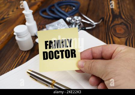 Concetto medico. Sulla tabella c'è un taccuino, medicinali e uno stetoscopio, nelle mani di un adesivo con l'iscrizione - MEDICO DI FAMIGLIA Foto Stock