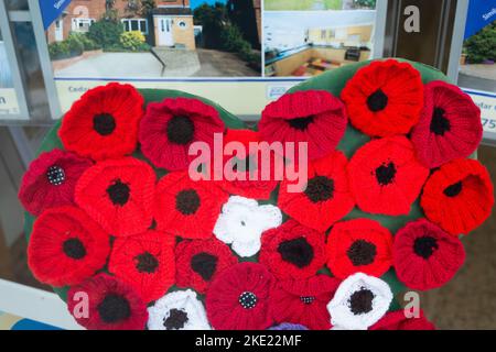 Bagshot, Surrey, Regno Unito. 7th Novembre 2022. Una vivace esposizione di papaveri lavorati a maglia nella finestra di un Agente Immobiliare a Bagshot High Street in memoria di coloro che hanno dato la loro vita per la nostra libertà. Credito: Maureen McLean/Alamy Foto Stock