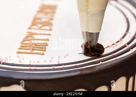 Decorazione di una torta bianca di compleanno con glassa al cioccolato Foto Stock