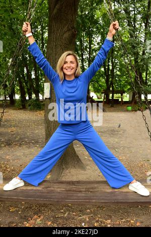 Giovane bella donna bionda di razza bianca si alza con i piedi su un'oscillazione di legno con le gambe larghe a parte Foto Stock