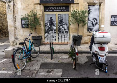 Due biciclette e uno scooter parcheggiati davanti a un poster di una mostra di fotografia di strada di Etienne Racine ad Arles, Francia. Foto Stock