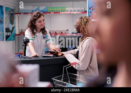 Farmacia cliente che paga trattamento di farmaci utilizzando terminale per il pagamento senza contatto con il telefono durante la consultazione medica in farmacia. Donna che acquista integratori sanitari, vitamina Foto Stock