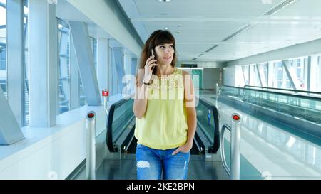 Donna in piedi sulla passerella automatica, in metropolitana attraversando, parlando, utilizzando il suo telefono, un mezzo di comunicazione, gadget. Il concetto è sempre in contatto. Foto di alta qualità Foto Stock