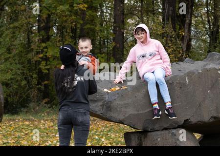 Una madre e i suoi due figli giocano sulle rocce in un parco in autunno. Foto Stock
