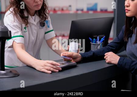 Cliente farmacia che paga il trattamento con la carta di credito durante la consultazione medica in farmacia. Il cliente acquista supplementi utilizzando il pagamento contactless. Assistenza sanitaria Foto Stock