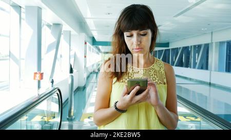 Donna in piedi sulla passerella automatica, scale in metropolitana attraversando, utilizzando il suo telefono, un mezzo di comunicazione, un gadget alla moda. Il concetto è sempre in contatto. Foto di alta qualità Foto Stock