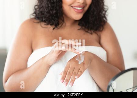 Colpo di primo piano di nero più taglia donna applicando crema idratante sulle mani, utilizzando lozione nutriente per la pelle secca Foto Stock