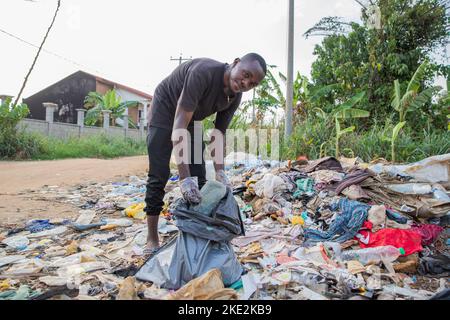 Il giovane uomo africano guarda la telecamera mentre raccoglie i rifiuti da terra. Foto Stock