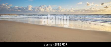 Vista panoramica della spiaggia di Cotton Tree surf nel bagliore dorato della mattina presto dopo l'alba. Le onde sono ruvide e si rompono ferocemente sulla sabbia Foto Stock