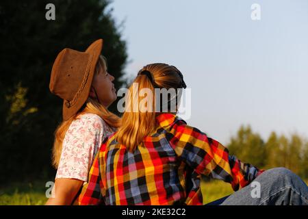 Sfocate la vista posteriore di madre e figlia seduti sul prato e guardando il campo verde. Concetto di amore di amicizia. Donna e ragazza sfondo estivo. Fuori Foto Stock