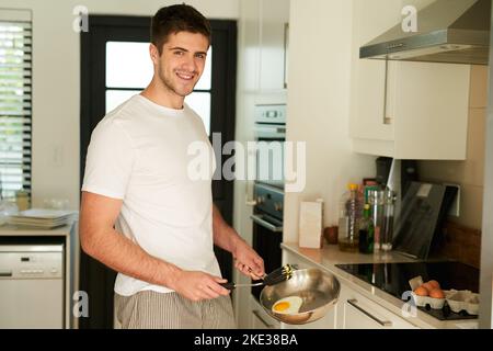 Mi piacciono le mattine al sole, un giovane che friggerà un uovo per la colazione a casa. Foto Stock