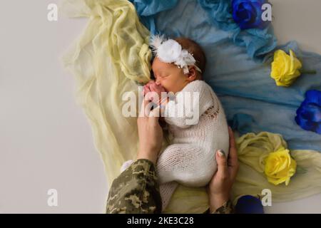 Neonato ucraino in studio colori blu giallo patriottico durante la guerra in Ucraina 2022. Un bambino piccolo, la ragazza dorme con la madre militare Foto Stock