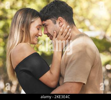 Coppia, abbraccio e fronte toccare con sorriso sul viso in natura, parco o all'aperto insieme per il legame. Giovane amore, uomo e donna da alberi con felicità Foto Stock