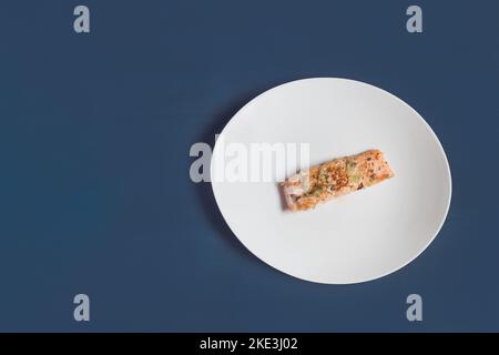 Una vista dall'alto di una porzione di un lombo di salmone al limone con prezzemolo e aglio su un piatto bianco e sfondo blu textured studio. Pesce e cibo. Foto Stock