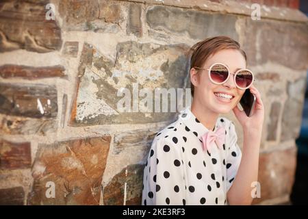 I suoi amici sanno come raggiungerla. Ritratto di una giovane donna alla moda che usa il telefono mentre si appoggia a una parete esterna. Foto Stock