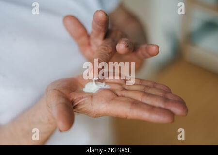 Vista ravvicinata della mano di una donna anziana che tiene la crema che deve applicare sul suo corpo. Trattamento di bellezza. Primo piano ritratto. Cura della pelle. Cura del corpo. Foto Stock