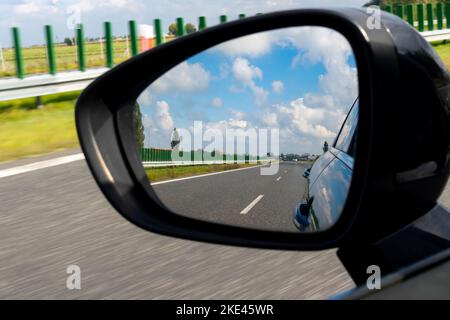 Vista nello specchietto retrovisore laterale di un'autovettura. Foto scattata durante la guida. Carreggiata sfocata sullo sfondo. Foto scattata in illuminazione naturale con Foto Stock