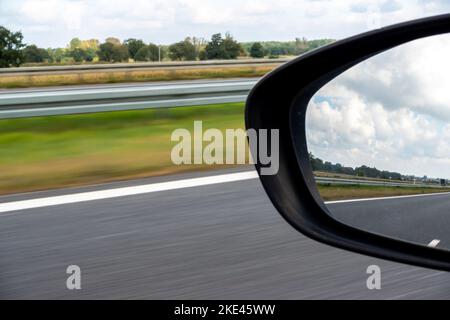 Vista nello specchietto retrovisore laterale di un'autovettura. Foto scattata durante la guida. Carreggiata sfocata sullo sfondo. Foto scattata in illuminazione naturale con Foto Stock