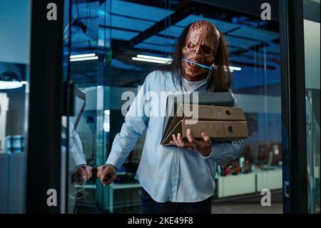 Zombie dipendente che trasporta la pila di raccoglitori cartella in ufficio Foto Stock