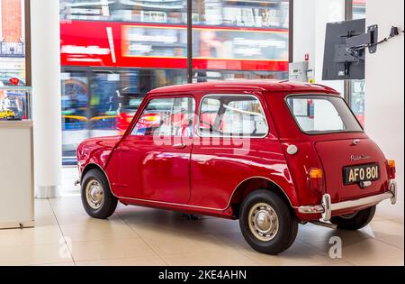 Un mini Austin originale splendidamente restaurato è parcheggiato in uno showroom nell'estremità ovest. Il mini è parcheggiato da una grande finestra mentre un autobus rosso passa accanto Foto Stock