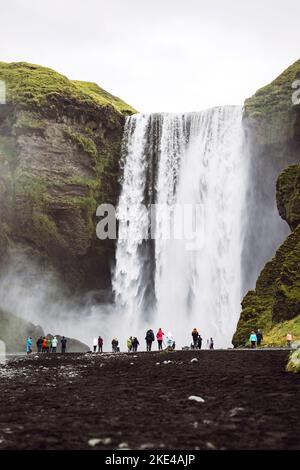 Attrazione turistica - cascata Skogafoss, colpo verticale di cascata dietro i turisti Foto Stock