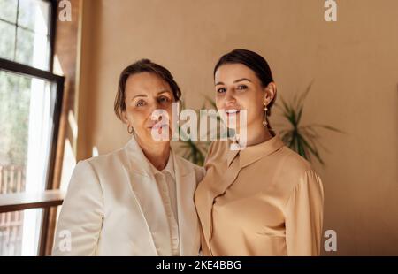Testa ripresa ritratto felice due generazioni di donne abbracciare, in piedi a casa, sorridendo madre anziana matura abbracciare bella figlia ringhiera da b Foto Stock