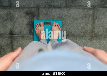 Uomo in piedi sulla bilancia. Piedi maschili su bilance di vetro, dieta maschile, peso corporeo, primo piano, uomo che sale su bilance, vista laterale Foto Stock