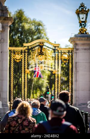 I turisti si affollano a Londra per visitare Buckingham Palace. Qui una guida con una bandiera Union Jack la alza in alto sopra la folla per i seguenti turisti Foto Stock