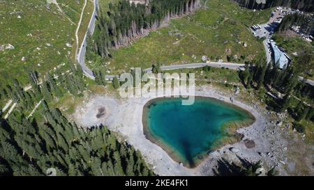 Un'immagine aerea del lago di Karersee, il Lago di Carezza con acque verde smeraldo, circondato da abeti in Italia Foto Stock