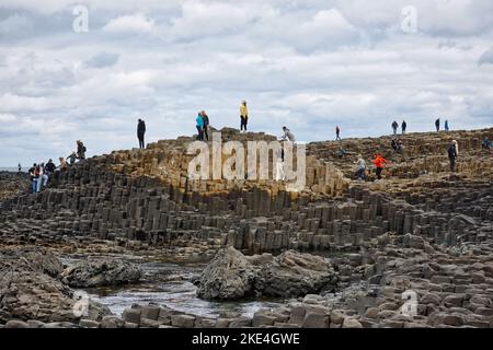 I turisti che si arrampicano sulle antiche colonne basaltiche del Selciato del gigante, patrimonio dell'umanità dell'UNESCO, Causeway Coast, County Antrim, Irlanda del Nord Foto Stock
