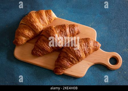 Tre croissant si trovano su un asse di legno su sfondo blu. Foto Stock