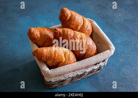 Quattro croissant in un cestino di vimini su sfondo blu Foto Stock