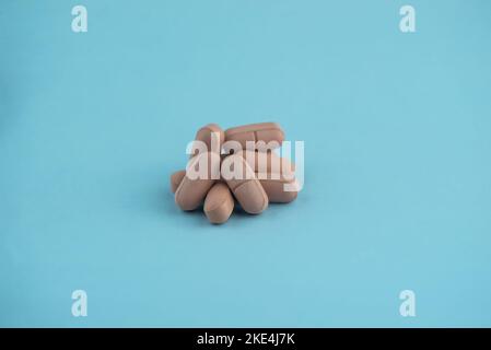 Semplice pila di pillole marroni. Medicinali, pillole impilate su sfondo blu. Forniture mediche. Foto Stock