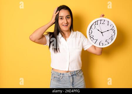 Giovane bella ragazza che tiene un grande orologio su sfondo giallo isolato molto felice ed eccitato, espressione del vincitore che celebra la vittoria urlando w Foto Stock