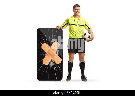 Ritratto a tutta lunghezza di un arbitro di calcio in piedi accanto a uno smartphone con schermo rotto fisso con bendaggio isolato su sfondo bianco Foto Stock