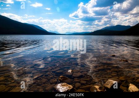 Un lago roccioso limpido con alte colline e nuvole bianche galleggianti in lontananza Foto Stock