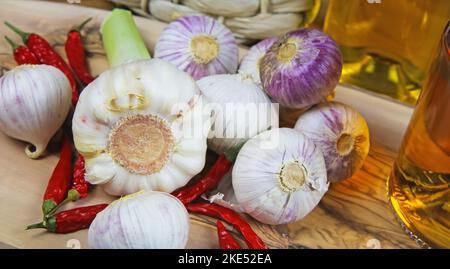 Isolato solo spicchio d'aglio e bulbo fresco su tagliere di legno d'oliva, peperoncini e bottiglie di vetro d'olio Foto Stock