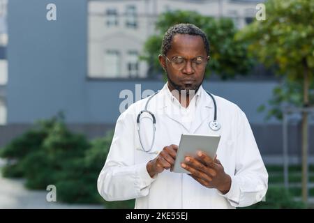 Ritratto di serio e concentrato medico sul lavoro, afro-americano uomo in occhiali di lavoro con tablet computer al di fuori della clinica. Foto Stock