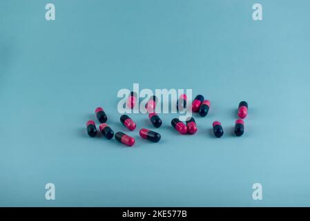 Semplice pila di pillole rosa e nere. Medicinali, pillole impilate su sfondo blu. Forniture mediche. Foto Stock