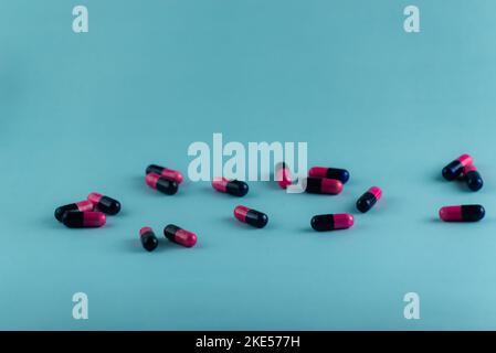 Semplice pila di pillole rosa e nere. Medicinali, pillole impilate su sfondo blu. Forniture mediche. Foto Stock