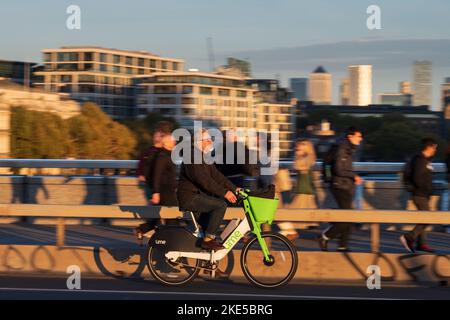 Un uomo che si trova a Londra durante l'ora di punta e che si trova a Londra durante il viaggio in bicicletta elettrica a noleggio. London Bridge, Londra, Regno Unito. 28 Ott 2022 Foto Stock