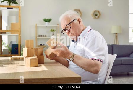 Uomo anziano dementato con malattia di Alzheimer seduto al tavolo e giocando con cubi di legno Foto Stock