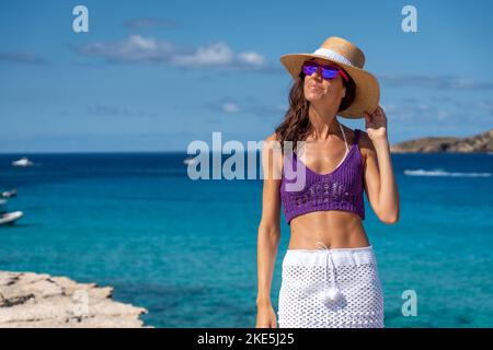 Un'attraente femmina caucasica con una gonna bianca e una parte superiore viola sulla spiaggia in una giornata di sole Foto Stock